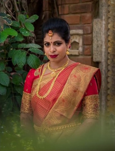 Shobana in a red and gold silk saree with temple jewellery, photographed among green leaves